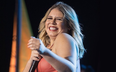 Marília Mendonça usa top laranja e sorri durante show em foto publicada no site oficial da cantora