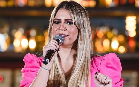 Com blusa rosa, Marília Mendonça canta durante show