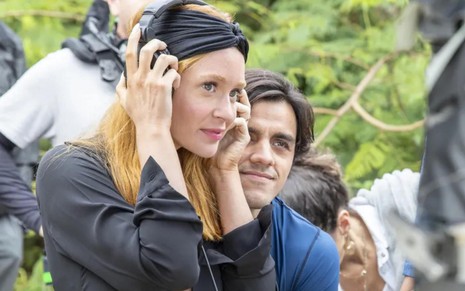 Marina Ruy Barbosa e Felipe Simas nos bastidores de gravações da novela Fuzuê, Marina segurando fones de ouvido na cabeça, Simas ao lado dela, observando