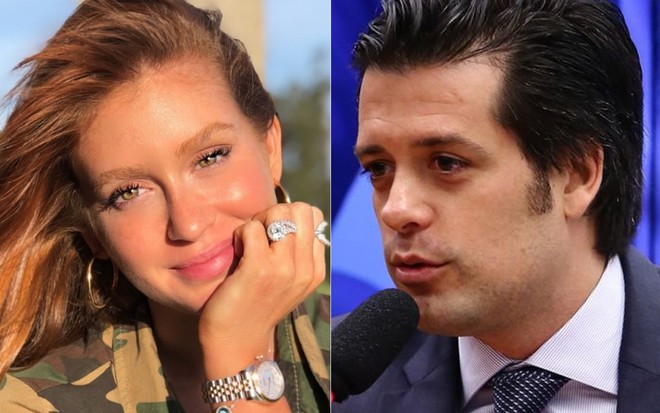 Marina Ruy Barbosa com a mão apoiada no queixo e camisa camuflada; Guilherme Mussi de terno e gravata falando ao microfone