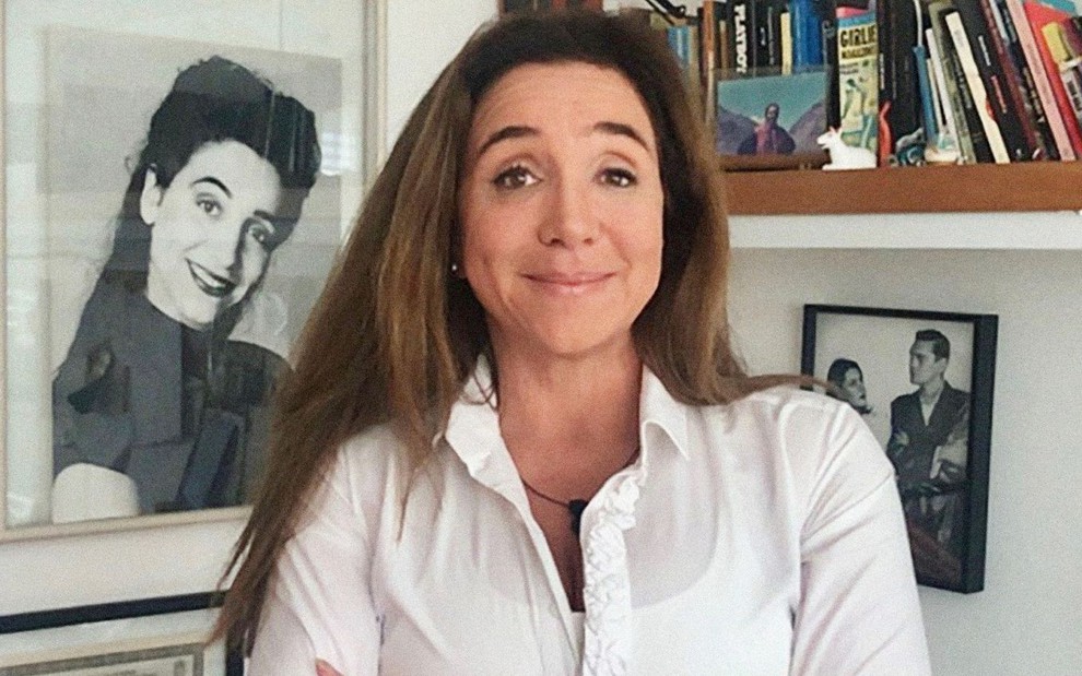 Marisa Orth sorri e está em frente a quadros e uma estante em foto de divulgação da temporada de 2020 do Zorra