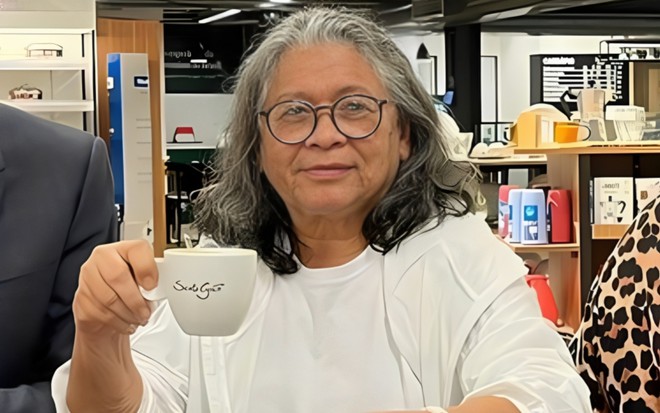 Marlene Mattos sorri e está com uma xícara de café nas mãos
