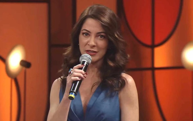 Ana Paula Padrão com um vestido azul e segurando um microfone no cenário do MasterChef em 2021