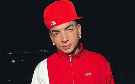 Foto de MC Guimê; ele veste jaqueta vermelha e usa boné vermelho