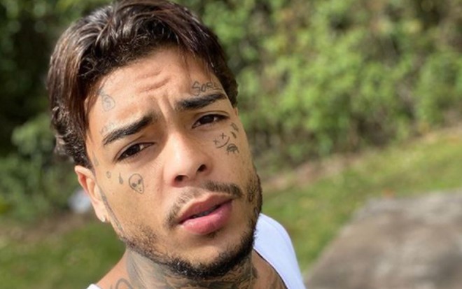 MC Kevin com o rosto tatuado, cabelo alisado e regata branca