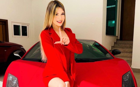 MC Melody faz a letra L com a mão; cantora veste terninho vermelho e está sentada em carro de luxo vermelho