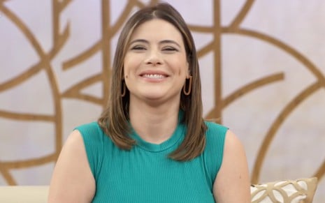 A apresentadora Michelle Loreto sorri no estúdio do Encontro, na Globo, de vestido verde