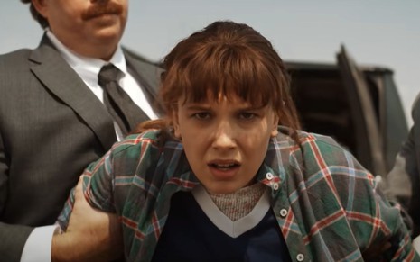 Millie Bobby Brown é segurada pelo braço em cena de Stranger Things