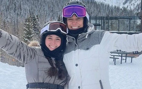 Mônica Martelli e a filha, Júlia, estão usando roupa para usar na neve: elas posam em uma estação de esqui
