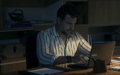 Em cena de Travessia, Rodrigo Lombardi está em seu escritório, mexendo no computador