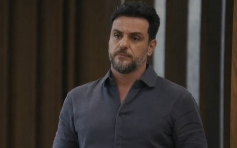 Em cena de Travessia, Rodrigo Lombardi está com a expressão de incômodo; ele usa camisa de botão na cor chumbo