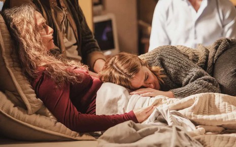 Lumiar (Carolina Dieckmann) chora abraçada ao corpo de Dora (Claudia Ohana) na cama em cena de Vai na Fé