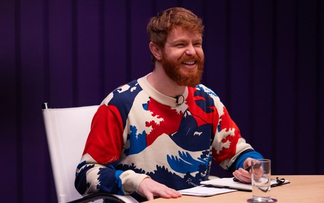 Com blusa colorida, Erick Krominski sorri abertamente na "Sala da Justiça" do Solução MTV