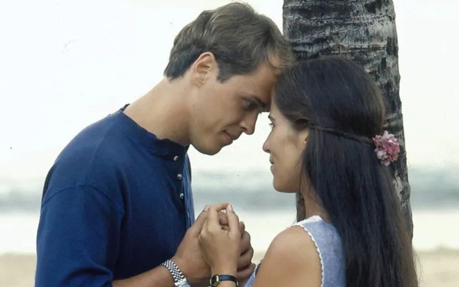 Na praia, Marcos (Guilherme Fontes) está de mãos dadas com Ruth (Gloria Pires) e encosta a testa na dela em cena da novela Mulheres de Areia (1993)