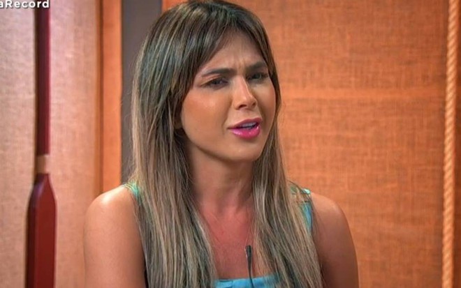 Nadja está sentada, veste regata azul e está na frente de uma parede madeira