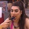 Naiara Azevedo comendo de boca aberta no BBB22, ela está sentada na cozinha vestindo uma regata rosa e com a boca cheia de comida