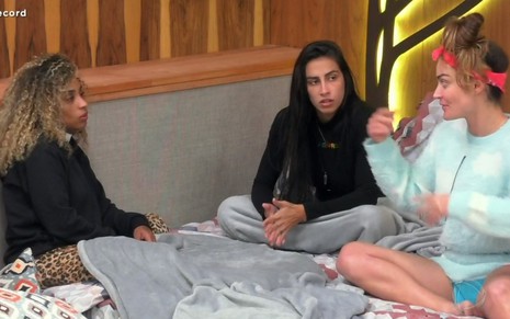 Nanah Damasceno, Any Borges e Laura Keller sentadas em uma cama, conversando