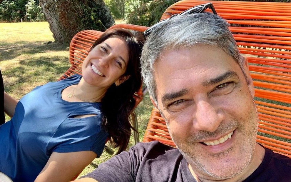 Selfie do âncora William Bonner com a mulher, Natasha Dantas, em um jardim; casal sorridente está em cadeiras laranjas