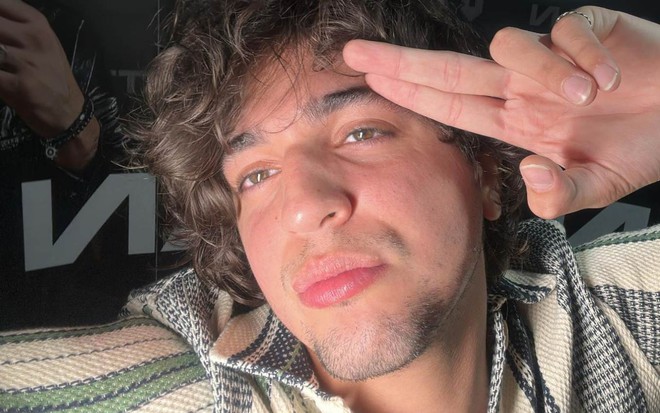 O cantor Nattanzinho em selfie com dois dedos na cabeça, expressão séria