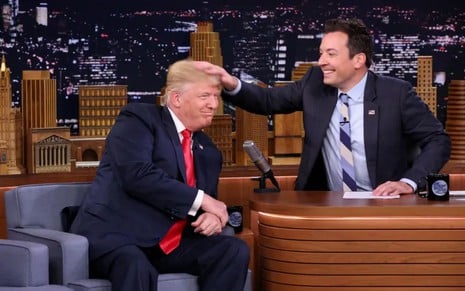 Jimmy Fallon sorri enquanto bagunça cabelo de Donald Trump no cenário do The Tonight Show