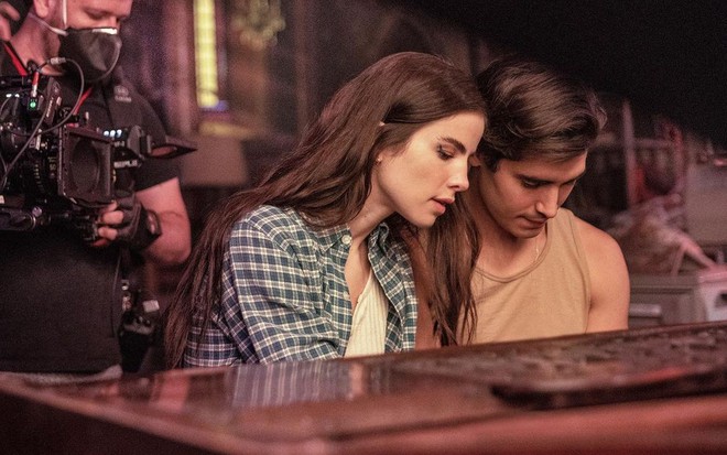 A cantora Giulia Be e o ator Henry Zaga estão dedilhando em um piano durante as gravações do novo filme da Netflix