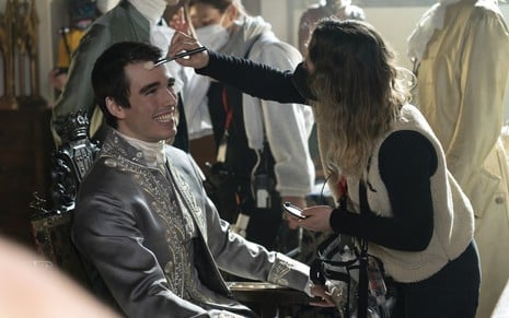 Corey Mylchreest sorri abertamente enquanto é maquiado nos bastidores de Rainha Charlotte