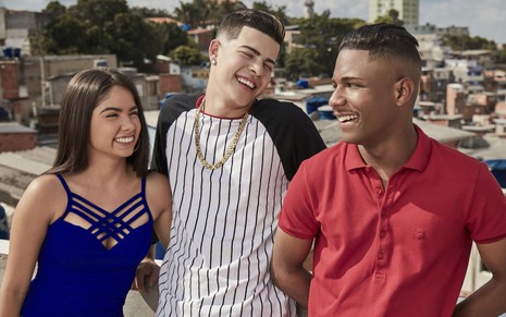 Bruna Mascarenhas, Jottapê e Christian Malheiros estão sorridentes no meio da favela de Sintonia, série da Netflix