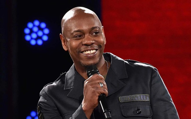 O comediante Dave Chappelle sorri com o microfone na mão no especial de stand-up Encerramento, da Netflix