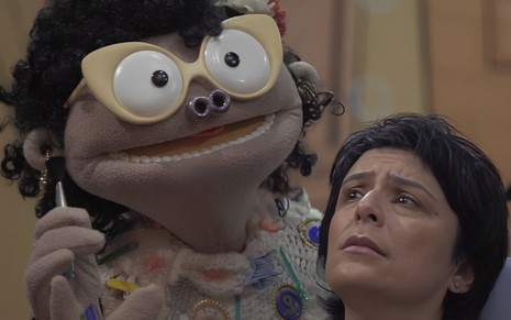Uma boneca gigante está maquiando a cantora Fernanda Takai em cena da série Música de Brinquedo