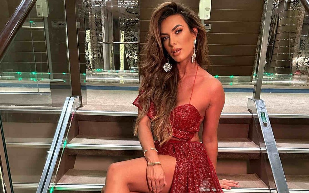Nicole Bahls posa de vestido de gala vermelho sentada em uma escada