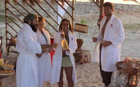 Quatro pessoas do No Limite 5 usando roupões de banho em uma tenda na praia