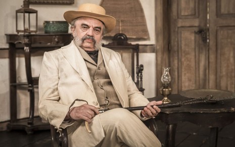 Coronel Eudoro (José Dumont) está sentado em cadeira com uma bengala no colo em cena de Nos Tempos do Imperador