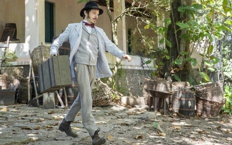 Nélio (João Pedro Zappa) anda em estrada de terra, com a casa dos pais ao fundo, em cena de Nos Tempos do Imperador
