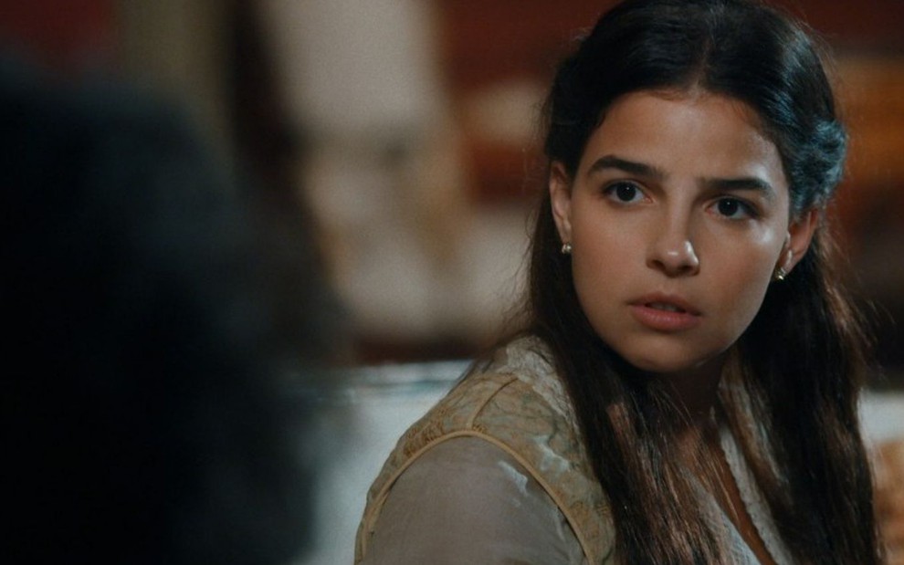 Pilar (Gabriela Medvedovski) está sentada na sala de dom Pedro 2º (Selton Mello) e tem expressão facial de surpresa em cena de Nos Tempos do Imperador