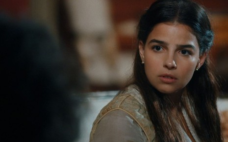 Pilar (Gabriela Medvedovski) está sentada na sala de dom Pedro 2º (Selton Mello) e tem expressão facial de surpresa em cena de Nos Tempos do Imperador