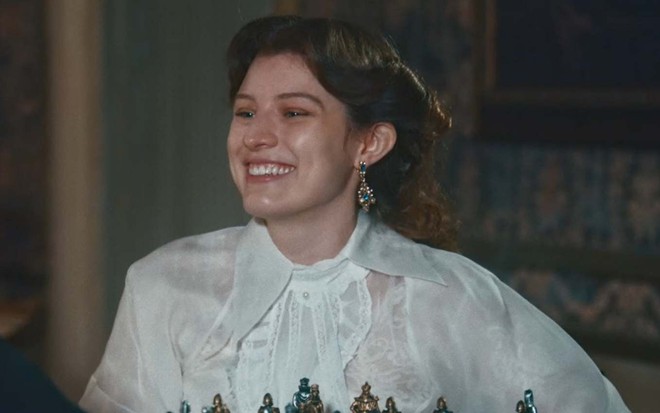 A atriz Giulia Gayoso olha para frente e sorri em cena de Nos Tempos do Imperador