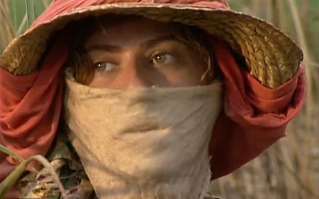 A atriz Patricia Pillar com pano no rosto, chapéu de palha, em meio a plantação de cana em cena de O Rei do Gado