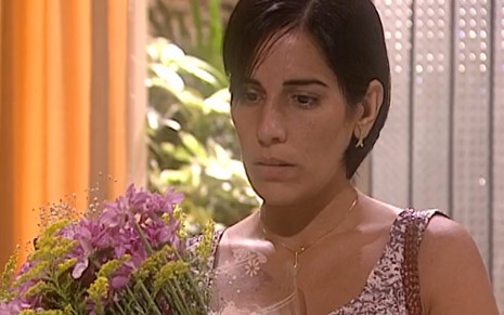 A atriz Gloria Pires com expressão séria, segurando buquê de flores em O Rei do Gado