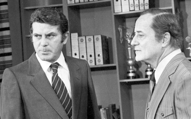 Os atores Carlos Zara e Paulo Autran em cena em preto e branco da novela Pai Herói, ambos com expressões sérias, de terno e gravata