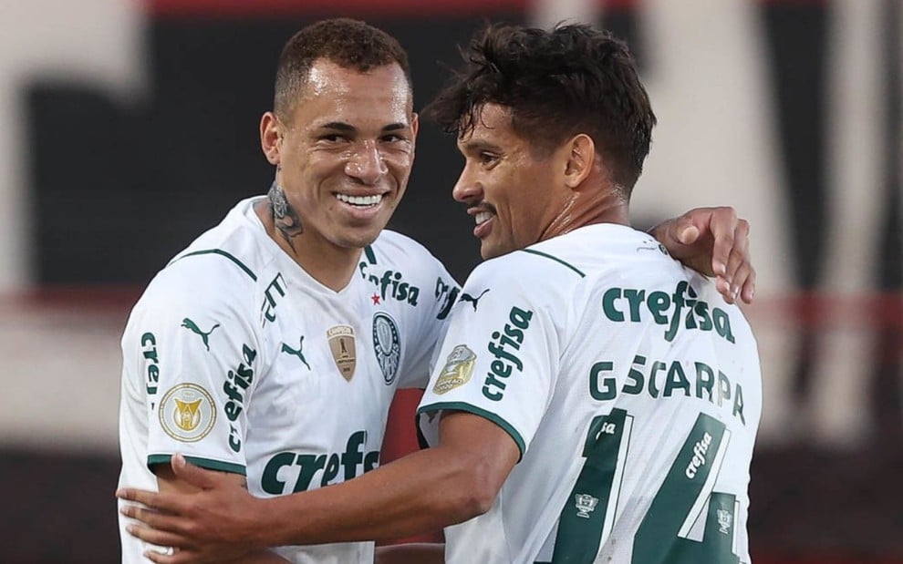Breno Lopes e Gustavo Scarpa do Palmeiras se abraçam e comemoram um gol da equipe no Campeonato Brasileiro. Eles usam a camisa branca do clube alviverde.