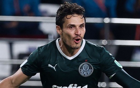 Raphael Veiga, do Palmeiras, veste uniforme verde com detalhes brancos e comemora gol de braços abertos