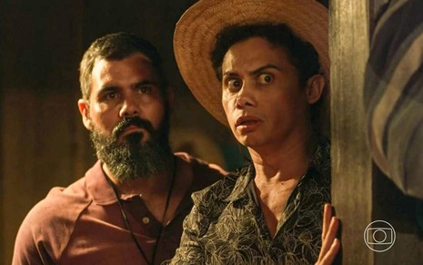 Os atores Juliano Cazarré e Silvero Pereira como Alcides e Zaquieu em Pantanal; eles estão em pé, olhando atentamente para frente com cara de assustados