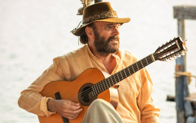 Almir Sater usa chapéu e segura violão em cena como Eugênio na novela Pantanal