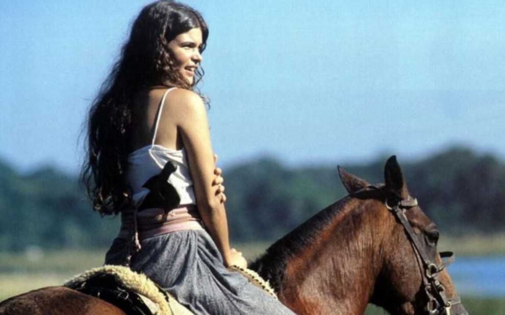 A atriz Cristiana Oliveira montada num cavalo, em paisagem de campo, em cena de Pantanal