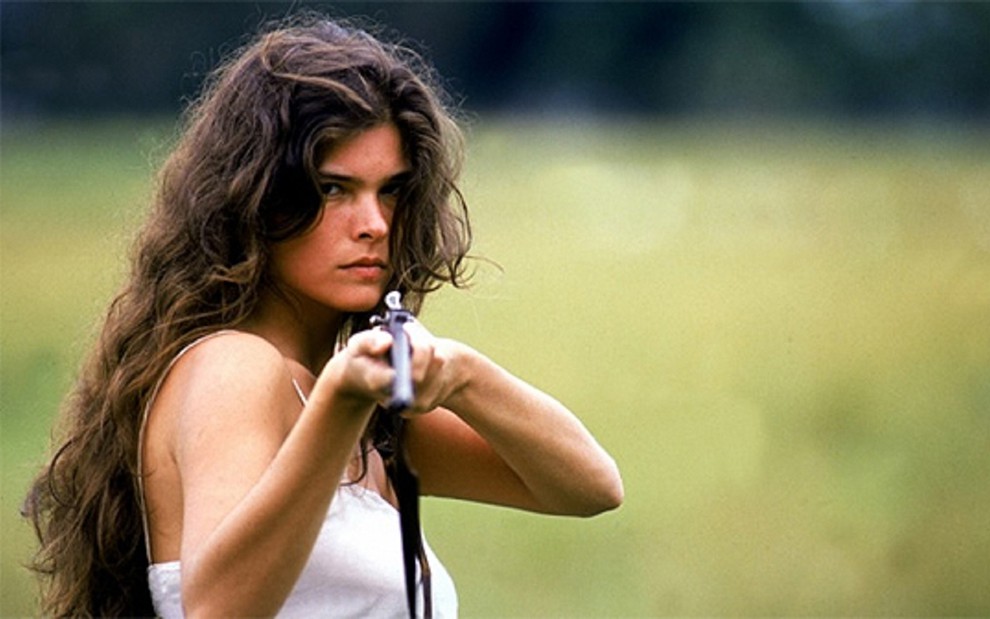 Cristiana Oliveira como Juma, no Pantanal, produzida pela Manchete em 1990: uma arma em punho e cabelo solto e longo. A atriz tinha 25 anos no papel