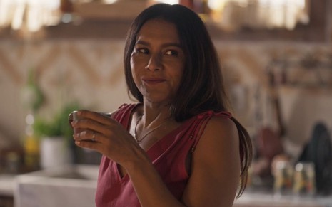 Filó (Dira Paes) dá um sorrisinho e segura uma xícara em cena da novela Pantanal