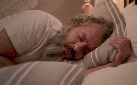 O ator Marcos Palmeira deitado numa cama, de olhos fechados, em cena de Pantanal
