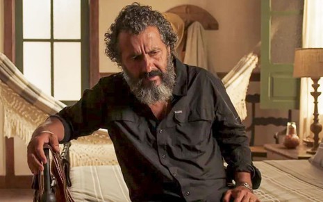 O ator Marcos Palmeira como José Leôncio em Pantanal; ele está sentado na cama e olhando para baixo, com a mão na cabeceira e com cara de preocupado