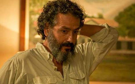 O ator Marcos Palmeira como José Leôncio em Pantanal; ele está olhando para baixo enquanto leva a mão esquerda para trás de sua cabeça