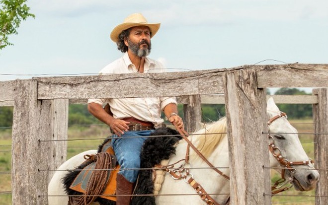 O ator Marcos Palmeira está caracterizado como seu personagem em Pantanal: ele usa chapéu, roupa de peão e está sentado em um cavalo